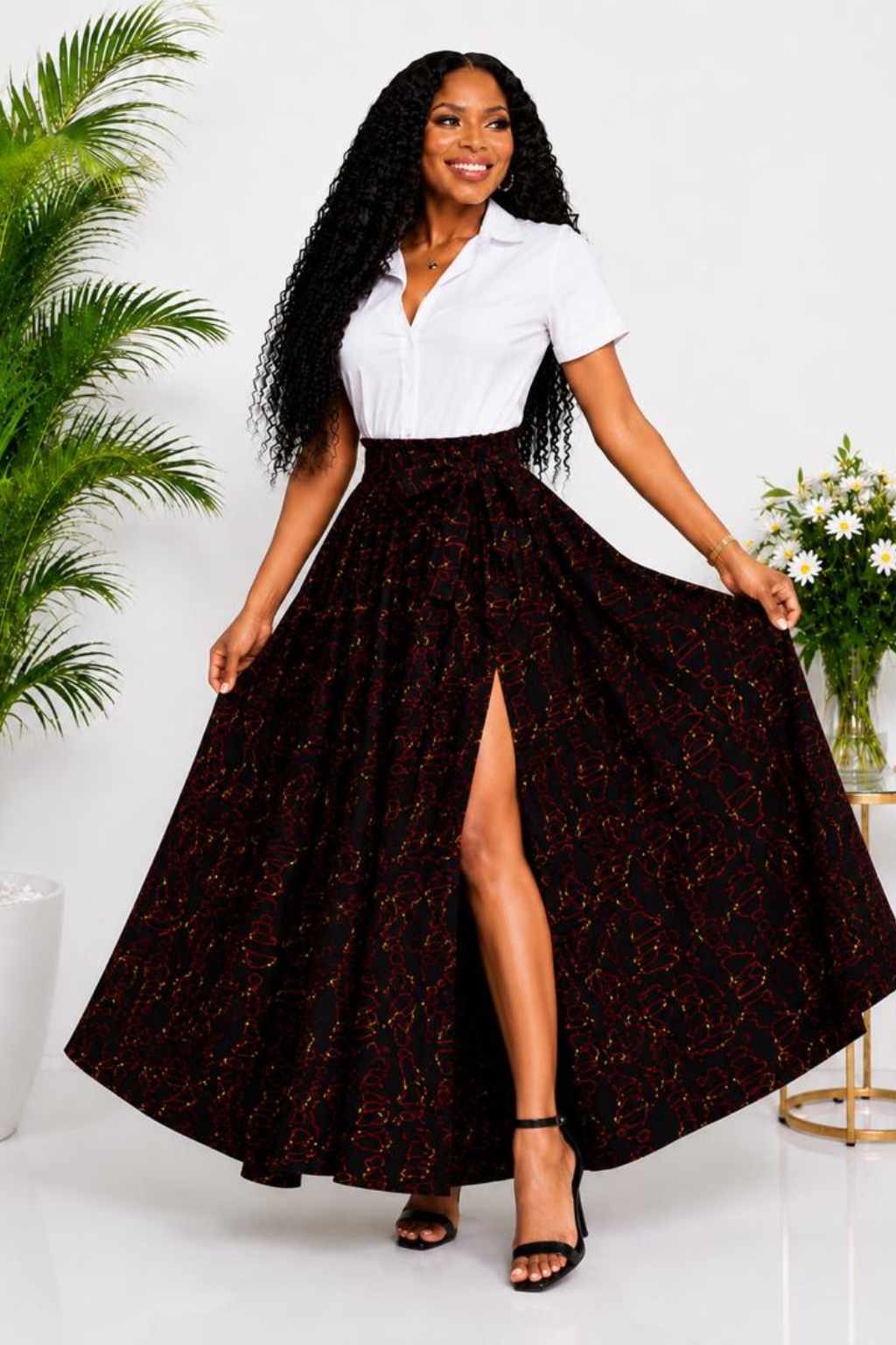 Woman wearing a black, red and gold abstract African print high-waisted pleated maxi skirt