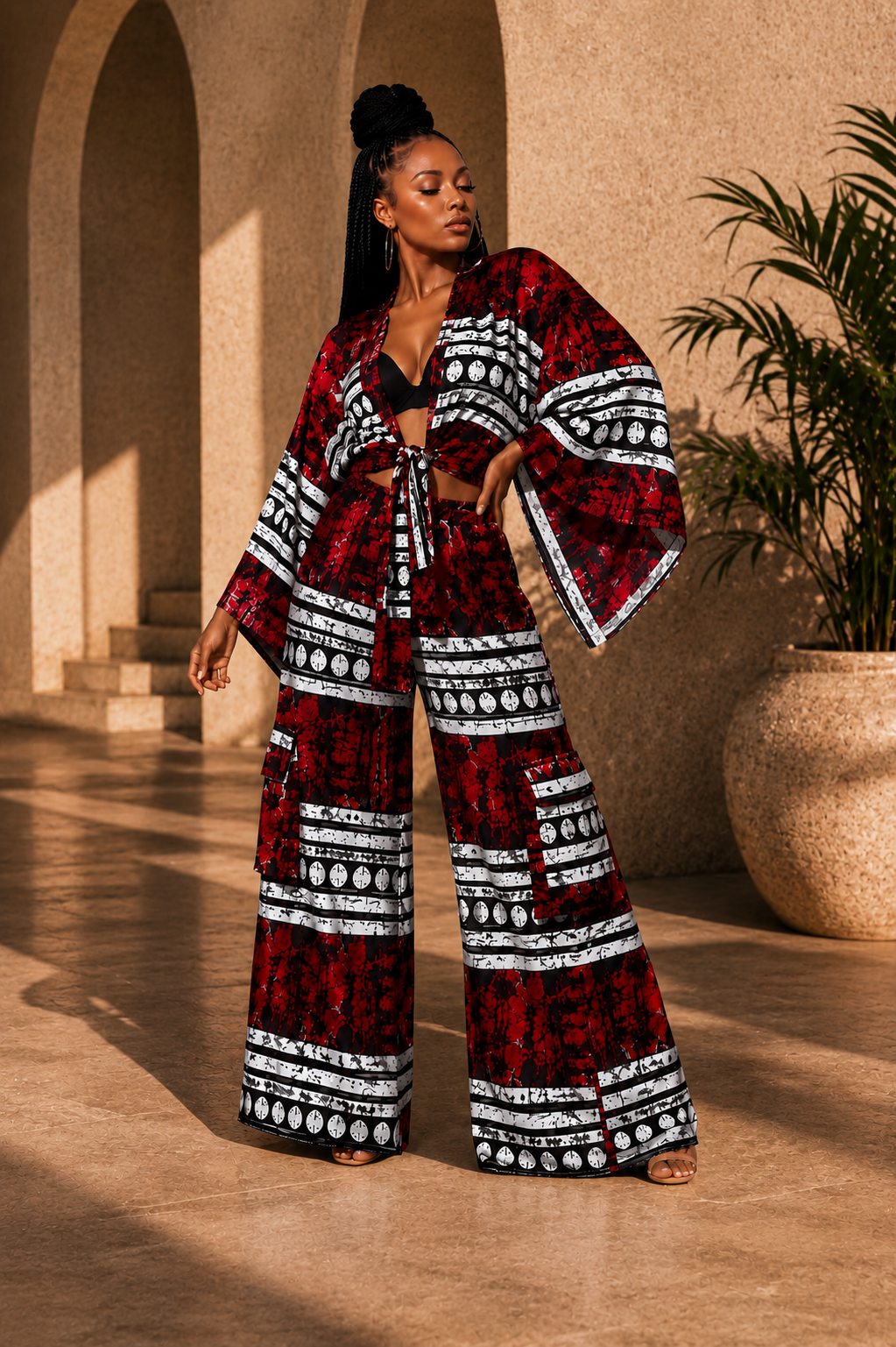Woman modeling a luxury red and black African print two-piece co-ord set with a wide-sleeve tie-front kimono top and matching high-waisted wide-leg palazzo pants.