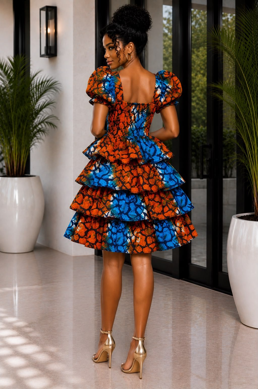African Print Smocked Puff Sleeve, Ankara Tiered Ruffle Mini & Blue and Orange Batik Layered Cocktail Dress. 2 Woman Wearing An African Print Smocked Puff Sleeve, Ankara Tiered Ruffle Mini & Blue and Orange Batik Layered Cocktail Dress.